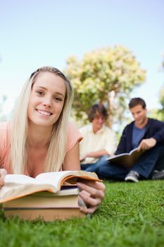 Portrait of a girl lying while reading books in a park with friends in background