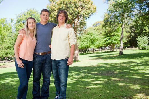Portrait of three smiling students shoulder to shoulder in a park