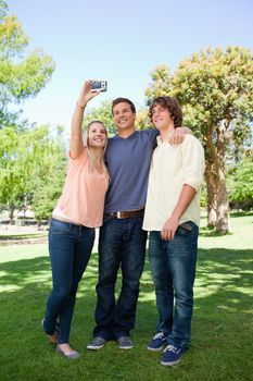 Three smiling students taking a pictures of themselves in a park