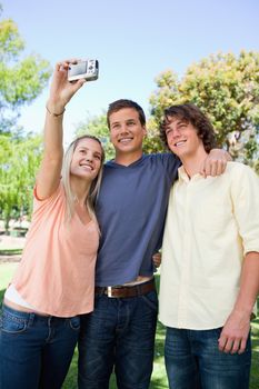 Three smiling friends taking a pictures of themselves in a park