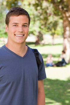 Portrait of a male student smiling in a park with friends in background