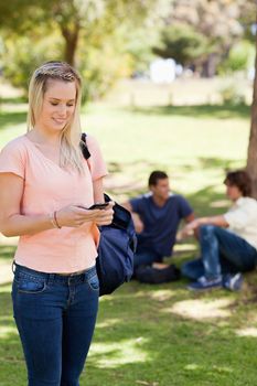 Standing girl using a smartphone in a park with friends in background