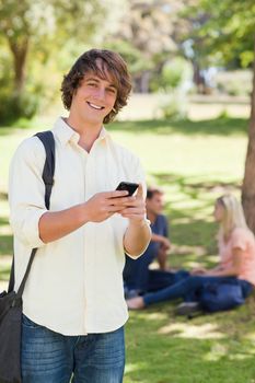 Portrait of a young man using a smartphone in a park with friends in background