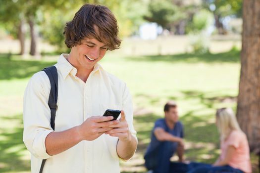 Close-up of a young man using a smartphone in a park with friends in background