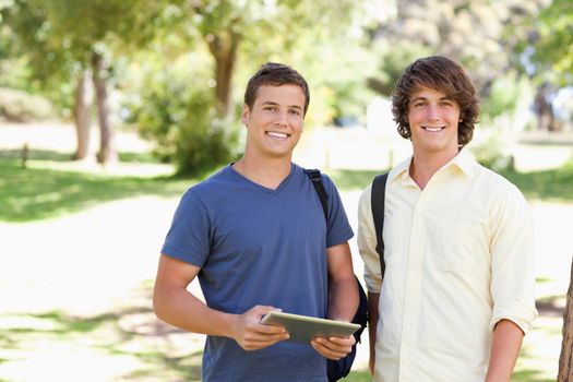 Close-up of two smiling male students with a touch pad in a park