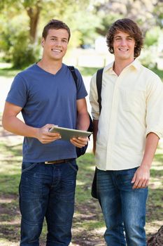 Portrait of two smiling male students with a touch pad in a park