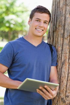 Close-up of a student leaning against a tree while using a touch pad in a park