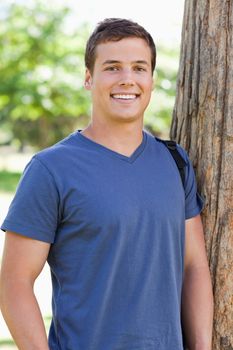 Close-up of a young man leaning against a tree in a park