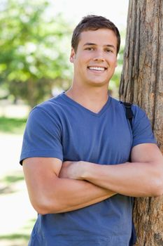 Close-up of a smiling young man leaning against a tree in a park