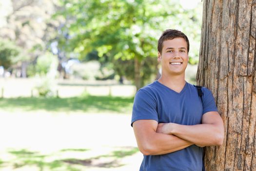 Portrait of a muscled student leaning against a tree in a park