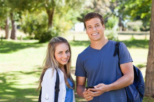 Portrait of a student showing his smartphone screen to a girl in a park