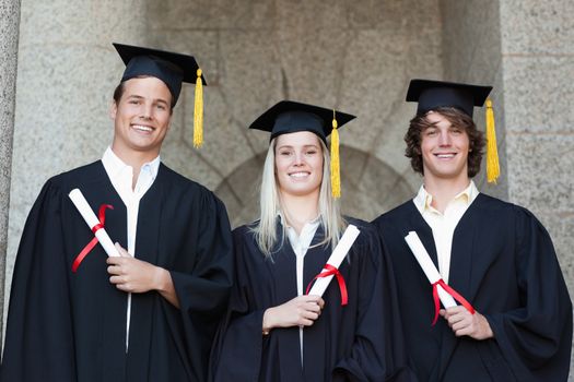 Graduates holding their diploma while posing with university in backgroung