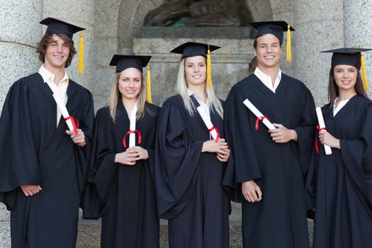 Smiling graduates posing in front of the university