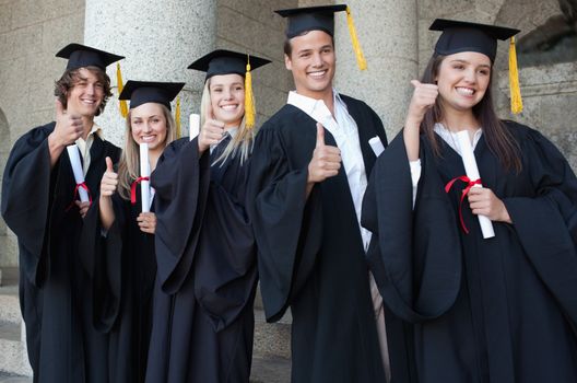 Graduates posing the thumb-up in front of the university