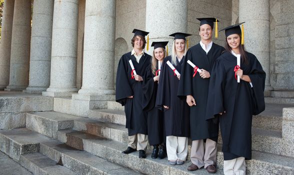 Five happy graduates posing in front of the university