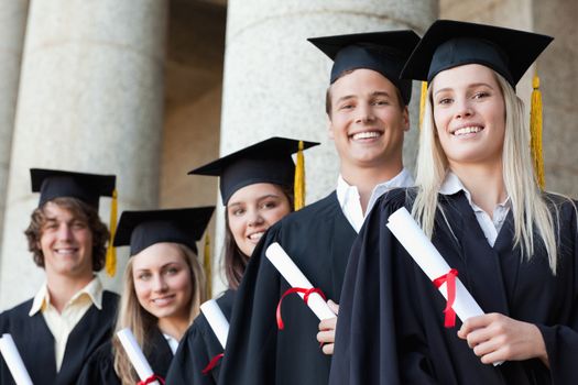 Close-up of five smiling graduates posing in front of the university