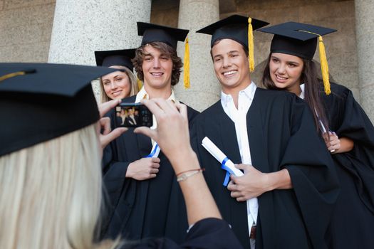 Close-up of a blonde graduate taking a picture of her friend in front of the university