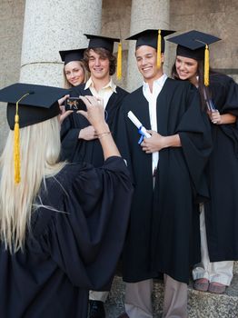 Blonde graduate taking a picture of her friend in front of the university