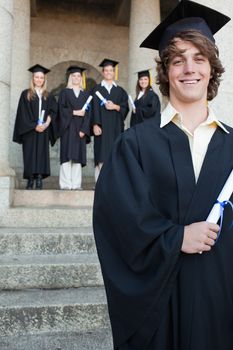 Close-up of a handsome graduate smiling with her friends in background in front of the university