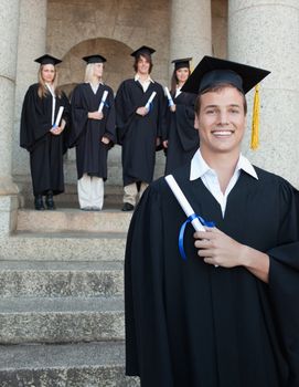 Close-up of a blue eyes graduate smiling with her friends in background in front of the university