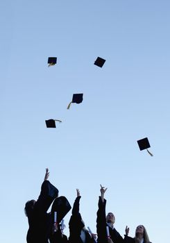 Low angle-shot of five grad students throwing their hats high in the sky 
