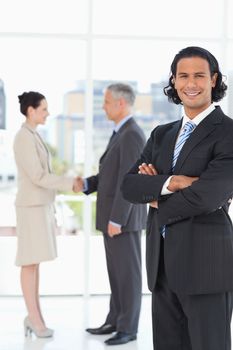 Young executive standing upright in front of business people shaking hands