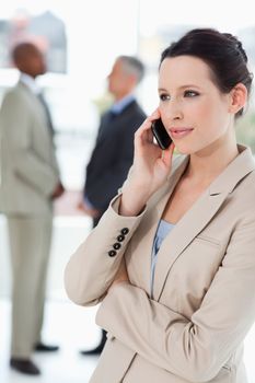 Serious businesswoman talking on a mobile phone with executives behind her