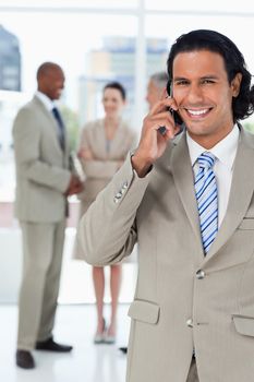 Young smiling executive talking on the phone and with his team behind him