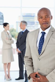 Young executive wearing a suit and crossing his hands with his team behind him