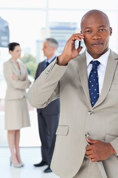 Young serious manager talking on the phone and while his team is behind him