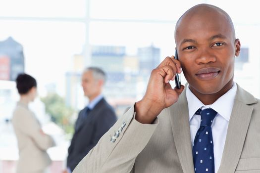 Young serious executive in a suit talking on the phone while his team stands behind him