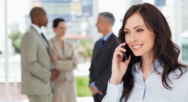 Executive woman talking on the phone in a relaxed way with her team behind her