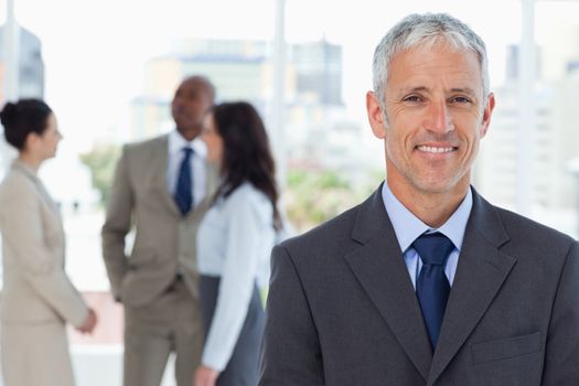 Mature smiling manager standing upright in front of his co-workers