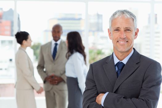 Mature smiling business manager crossing his arms in front of his business team