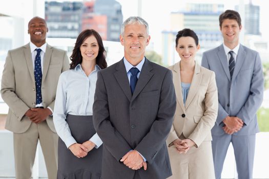 Mature businessman standing upright and followed by his smiling team