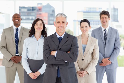 Mature businessman standing upright and crossing his arms in front of his team