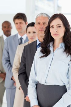 Young serious executive woman standing upright in front of her co-workers