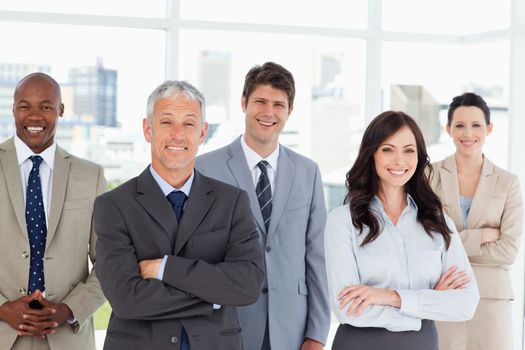 Five smiling business people crossing their arms in front of a bright window