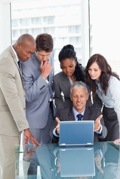 Mature businessman proudly showing the laptop screen to his team