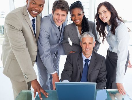 Mature businessman sitting at the desk surrounded by his smiling team 