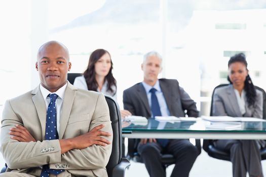 Young executive almost smiling and crossing his arms while his team is in the background