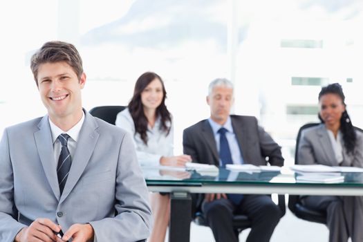 Smiling executive sitting in front of his earnest team and looking at the camera