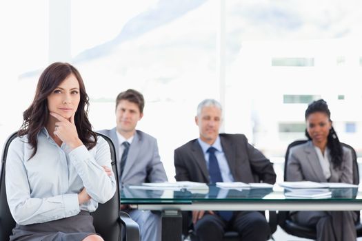 Confident businesswoman sitting with her hand on her chin in front of her serious team
