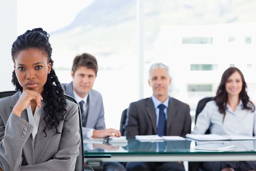 Young executive sitting with her hand on her chin in front of her team in a meeting room