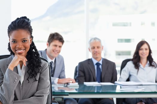Confident smiling executive sitting in a meeting room while her team is looking at her