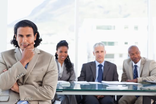 Stern businessman with his hand on his chin sitting in front of his business team