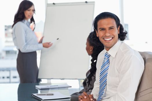 Smiling employee attending a presentation while his team is working behind him