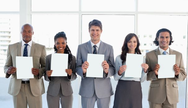 Business team standing upright side by side while showing blank sheets and smiling