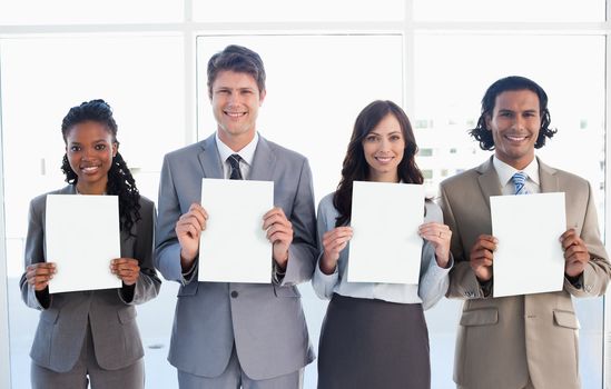 Smiling business people standing in front of a window while showing blank sheets