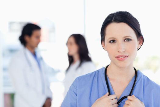 Serious intern looking at the camera while her medical team is in the background